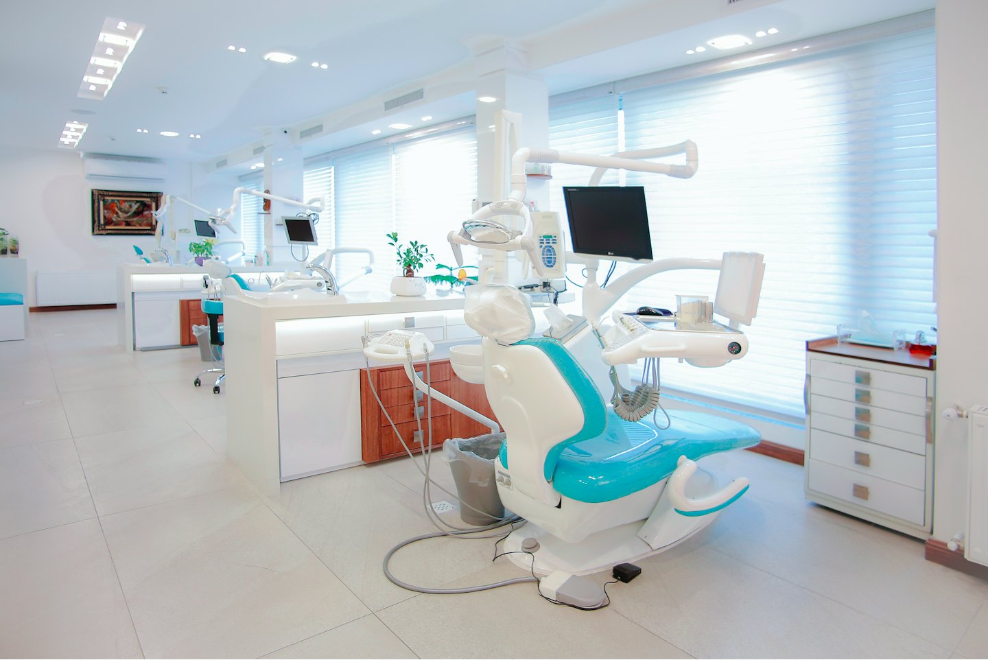Nowoczesne wnętrze kliniki dentystycznej z turkusowymi i białymi fotelami.